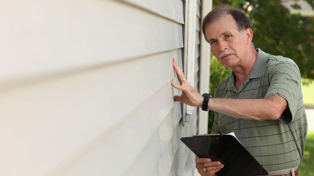 Inspecteur expliquant l'état de la toiture à un couple d'acheteurs devant une maison québécoise